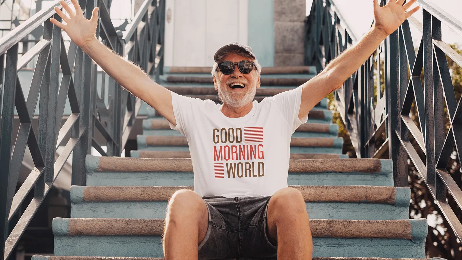 Mann mit Good Morning World Shirt sitzt auf der Treppe und freut sich
